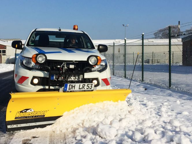Winterdienst: Räumfahrzeug mit gelber Schaufel schiebt Schnee im Winter; im Hintergrund: bluer Himmel und Industriegebiet Winterdienst: Räumfahrzeug mit gelber Schaufel schiebt Schnee im Winter; im Hintergrund: bluer Himmel und Industriegebiet